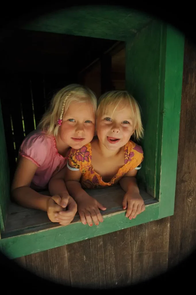 Zwei Mädchen schauen aus einem grünen Holzfenster - Urlaub in Schladming